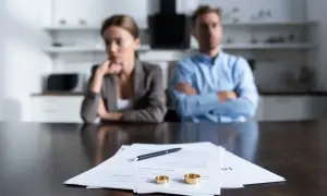 Para zamyślonych osób przy stole, na którym leżą dokumenty, długopis i obrączki.
