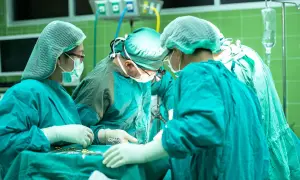 Zespół chirurgów w sterylnych strojach pracuje przy stole operacyjnym. W tle widać aparaturę medyczną. Sytuacja budzi niepokój, czy nieumyślne spowodowanie śmierci nie jest tu możliwe.