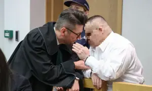 Prawnik pochyla się nad oskarżonym, omawiając, czy oskarżony może zobaczyć zeznania świadków.