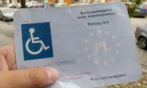 Karta parkingowa osoby niepełnosprawnej, z symbolem wózka inwalidzkiego, potwierdza stopień umiarkowany i uprawnia do parkowania.