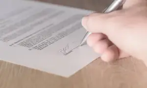 Dłoń podpisuje dokument srebrnym długopisem.