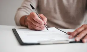 Dłoń pisze długopisem na dokumencie. To ważny wniosek o wydanie decyzji ustalającej poziom potrzeby wsparcia.