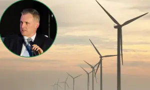 Mężczyzna w garniturze przemawia na tle farmy wiatraków. Dyskusja o ustawie wiatrakowej.