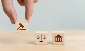 Dłoń układa kostki symbolizujące prawo, sprawiedliwość i sąd. Decyzja o jurysdykcji.