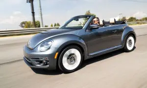 Szary kabriolet Volkswagen Beetle jedzie po drodze. Mężczyzna w okularach przeciwsłonecznych prowadzi auto. To idealny pojazd na letnie wycieczki, jak ta opisana w umowie użyczenia samochodu.