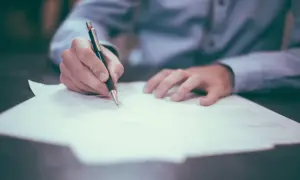 Dłoń pisze piórem na dokumencie. Może to oznaczać oddalenie wniosku przez sąd, gdy dokument jest odrzucany.