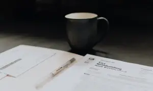 Kubek kawy i długopis leżą obok dokumentów podatkowych. Może to być duplikat faktury, który trzeba uzupełnić.