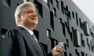 Uśmiechnięty mężczyzna w garniturze, właściciel firmy, trzyma telefon komórkowy na tle nowoczesnego budynku.