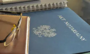 Akt notarialny z orłem, obok notes i okulary. To ważne dokumenty, tworzące repertorium prawnicze.