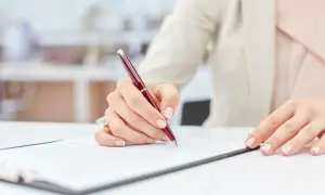 Dłoń podpisuje ważny dokument, być może weksel, na białym biurku.