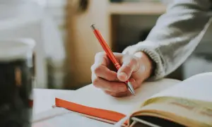 Dłoń pisze w notatniku, przygotowując się do egzaminu. Co to absolutorium? To zaliczenie, które otwiera drogę do dalszej nauki.