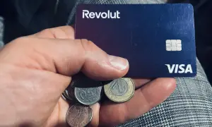 Dłoń trzyma kartę Revolut i polskie monety. Czy komornik może zająć konto Revolut? To pytanie nurtuje wielu.