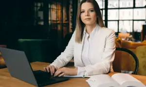 Kobieta w białej marynarce przy laptopie i otwartej księdze. Zastanawia się, jak zwracać się do adwokata, by uzyskać profesjonalną pomoc.