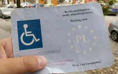 Karta parkingowa osoby niepełnosprawnej, z symbolem wózka inwalidzkiego, potwierdza stopień umiarkowany i uprawnia do parkowania.