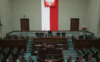 Pusta sala sejmowa, gotowa na głosowanie weta prezydenta. Biało-czerwona flaga i godło Polski na ścianie.