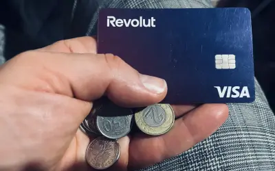 Dłoń trzyma kartę Revolut i polskie monety. Czy komornik może zająć konto Revolut? To pytanie nurtuje wielu.