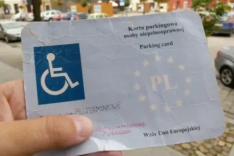 Karta parkingowa osoby niepełnosprawnej, z symbolem wózka inwalidzkiego, potwierdza stopień umiarkowany i uprawnia do parkowania.