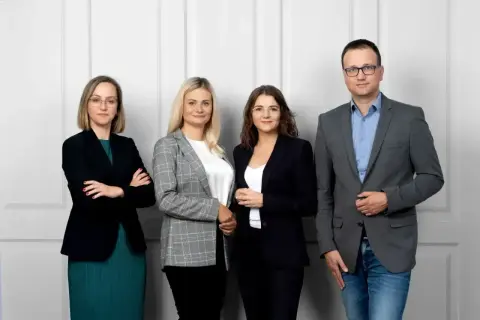 Cztery osoby w strojach biznesowych stoją przed jasną ścianą.