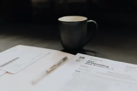 Kubek kawy i długopis leżą obok dokumentów podatkowych. Może to być duplikat faktury, który trzeba uzupełnić.