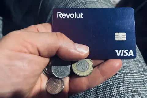 Dłoń trzyma kartę Revolut i polskie monety. Czy komornik może zająć konto Revolut? To pytanie nurtuje wielu.
