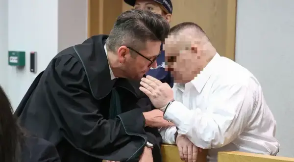 Prawnik pochyla się nad oskarżonym, omawiając, czy oskarżony może zobaczyć zeznania świadków.