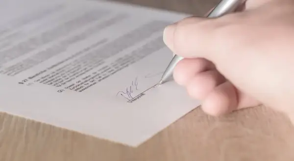 Dłoń podpisuje dokument srebrnym długopisem.
