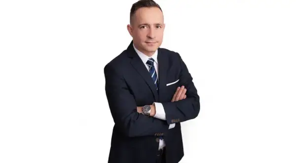 Mężczyzna w garniturze ze skrzyżowanymi rękami, na białym tle.