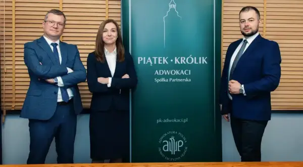 Trzy osoby w garniturach stoją przed zielonym banerem kancelarii Piatek-Krolik.