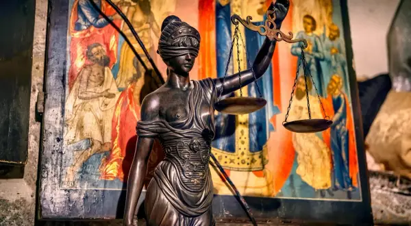 Posąg Temidy z wagą i opaską na oczach, symbol sprawiedliwości, stoi przed starą ikoną. Czy to zapowiedź wyroku nakazowego?