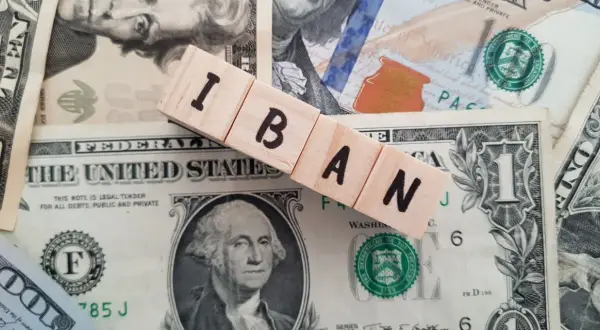 Drewniane klocki z literami IBAN leżą na banknotach dolarowych. IBAN to międzynarodowy numer rachunku bankowego.