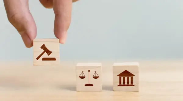 Dłoń układa kostki symbolizujące prawo, sprawiedliwość i sąd. Decyzja o jurysdykcji.