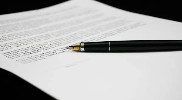 Czarny długopis na dokumencie z tekstem, który może zawierać klauzule abuzywne.