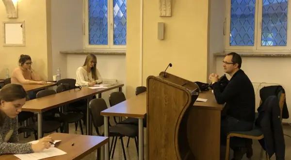 Referendarz sądowy prowadzi szkolenie. Kilka osób siedzi przy ławkach, słuchając i notując.