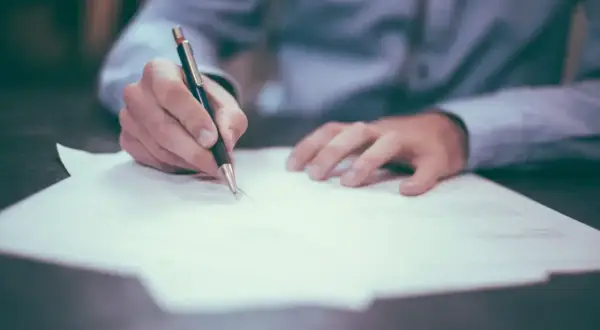 Dłoń pisze piórem na dokumencie. Może to oznaczać oddalenie wniosku przez sąd, gdy dokument jest odrzucany.