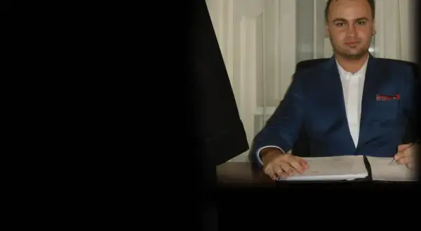 Mężczyzna w garniturze siedzi przy biurku z dokumentami.
