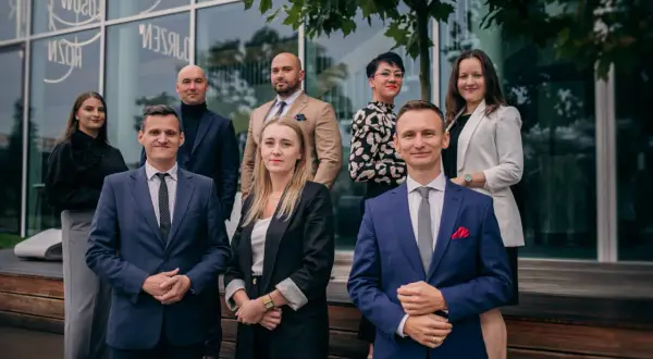 Grupa profesjonalistów w garniturach i eleganckich strojach pozuje przed nowoczesnym budynkiem.
