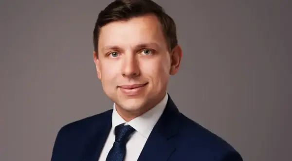 Portret mężczyzny w granatowym garniturze i krawacie na szarym tle.