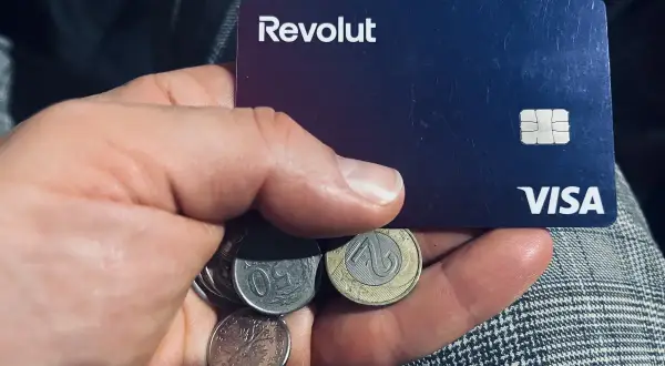 Dłoń trzyma kartę Revolut i polskie monety. Czy komornik może zająć konto Revolut? To pytanie nurtuje wielu.