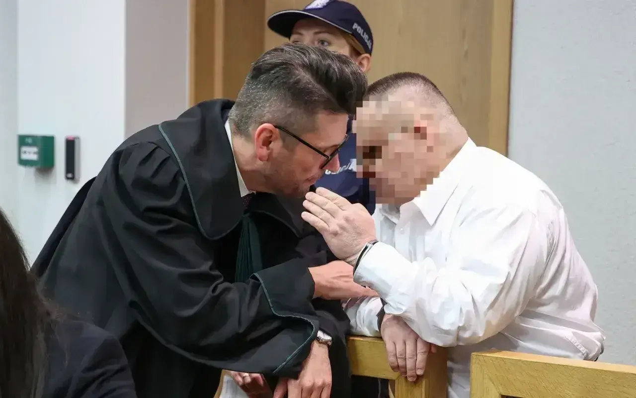 Prawnik pochyla się nad oskarżonym, omawiając, czy oskarżony może zobaczyć zeznania świadków.