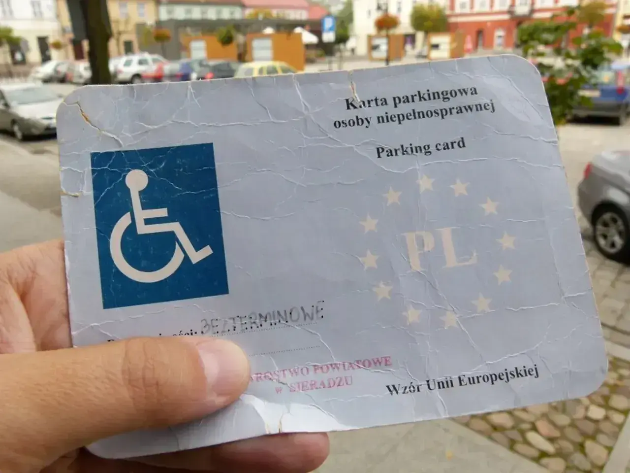 Karta parkingowa osoby niepełnosprawnej, z symbolem wózka inwalidzkiego, potwierdza stopień umiarkowany i uprawnia do parkowania.