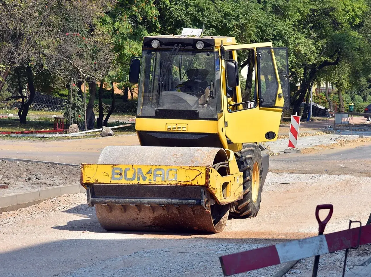 Żółty pojazd wolnobieżny, walec drogowy Bomag, pracuje na budowie drogi, ubijając nawierzchnię.