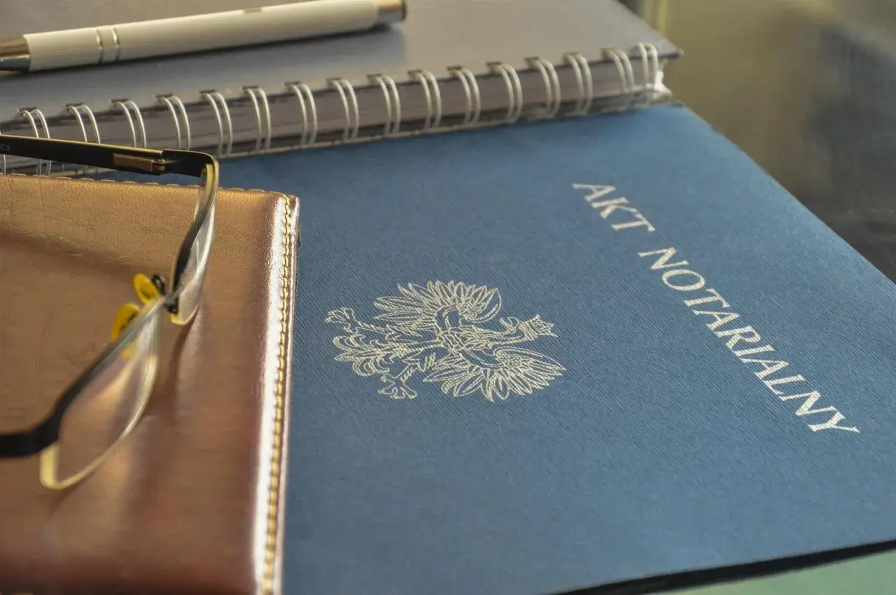 Akt notarialny z orłem, obok notes i okulary. To ważne dokumenty, tworzące repertorium prawnicze.