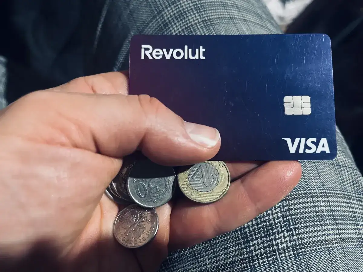 Dłoń trzyma kartę Revolut i polskie monety. Czy komornik może zająć konto Revolut? To pytanie nurtuje wielu.