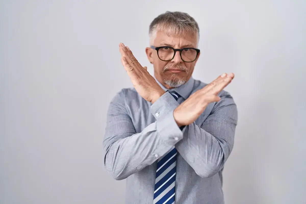 Mężczyzna w okularach z rękami skrzyżowanymi na piersi, gestem sugerującym odmowę. Czy pracodawca może odmówić urlopu na żądanie?
