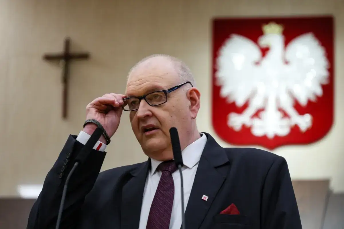Mężczyzna w garniturze, z okularami, przemawia. W tle godło Polski i krzyż. To część składu Trybunału Konstytucyjnego.