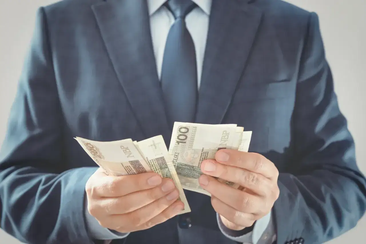 Mężczyzna w garniturze liczy banknoty 100 zł. Prawdopodobnie przygotowuje wadium na przetarg.