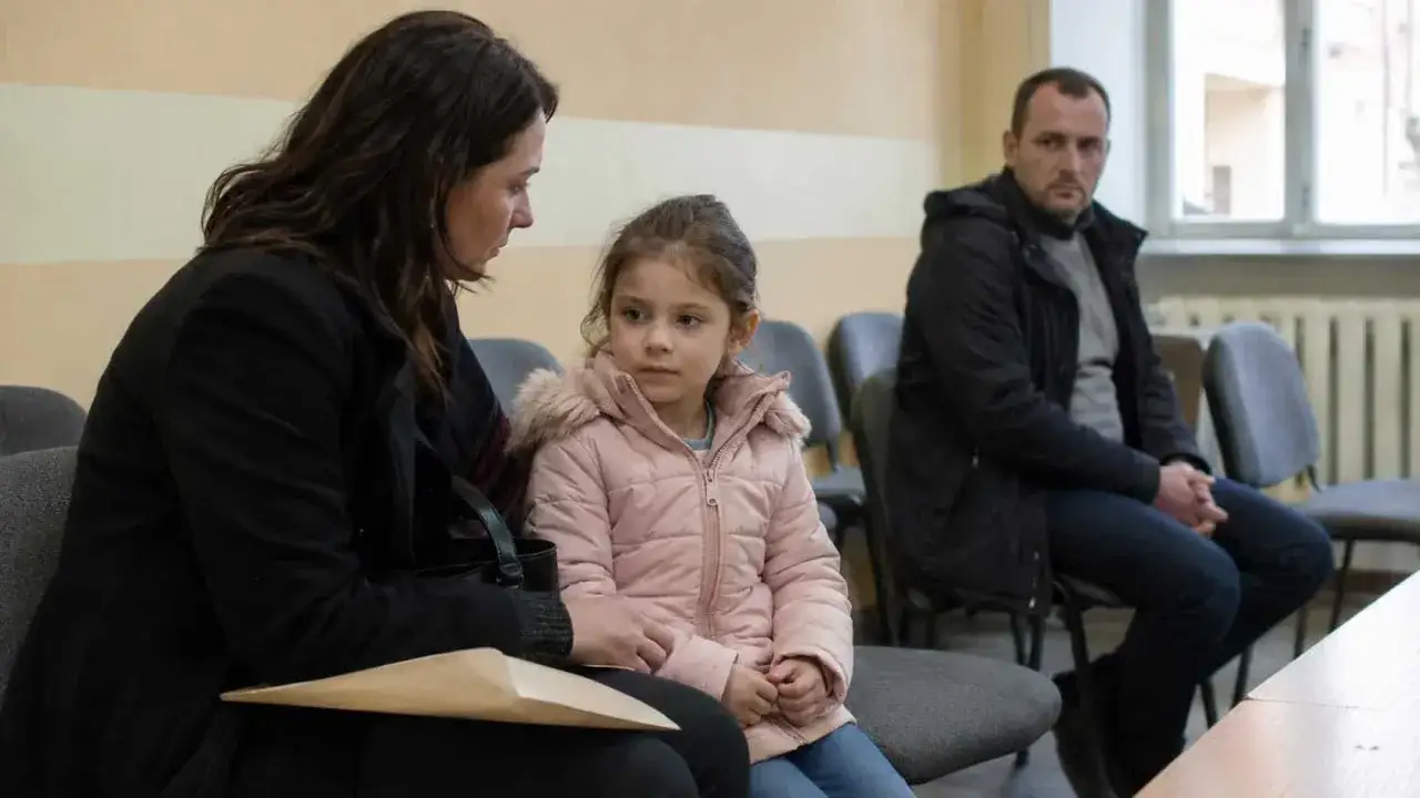 Matka z córką czekają na rozprawę. Czy sąd może zmusić dziecko do kontaktów z ojcem? Mężczyzna siedzi w tle.