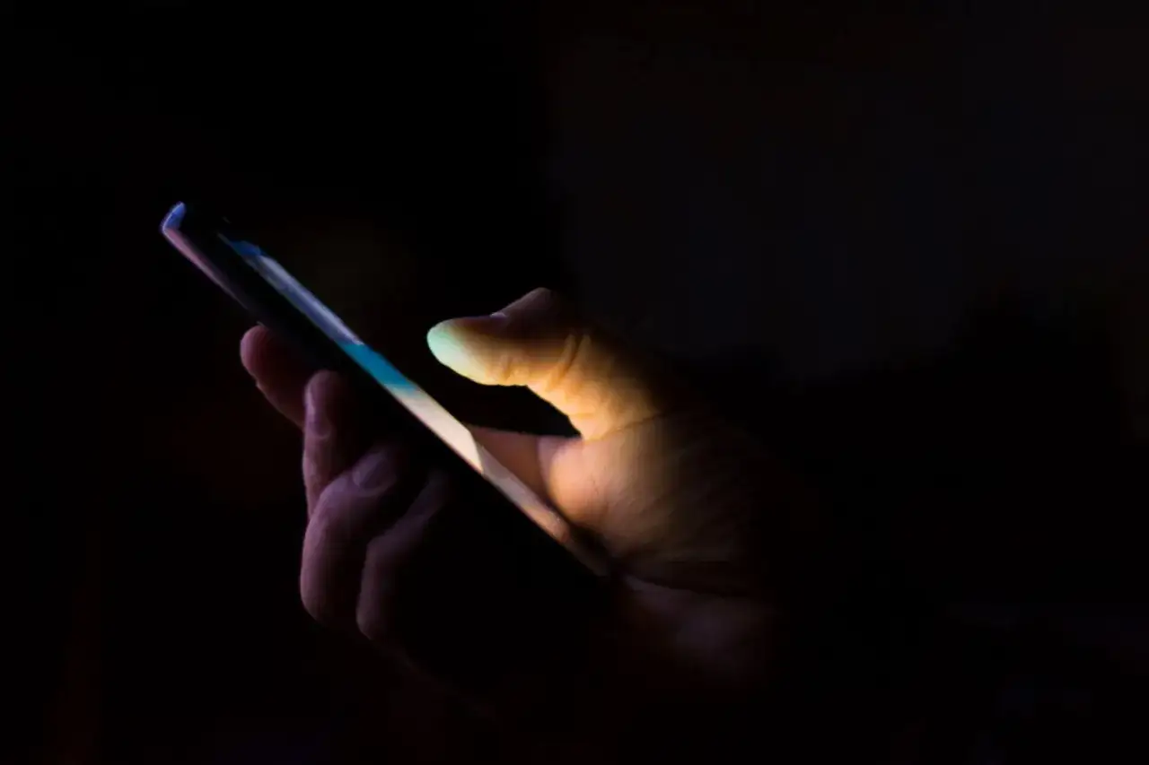 Dłoń trzyma smartfon w ciemności. Czy to stalker? Kto to?