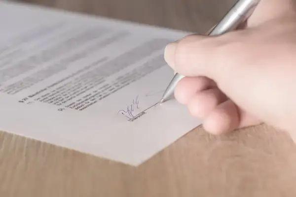 Dłoń podpisuje dokument srebrnym długopisem.
