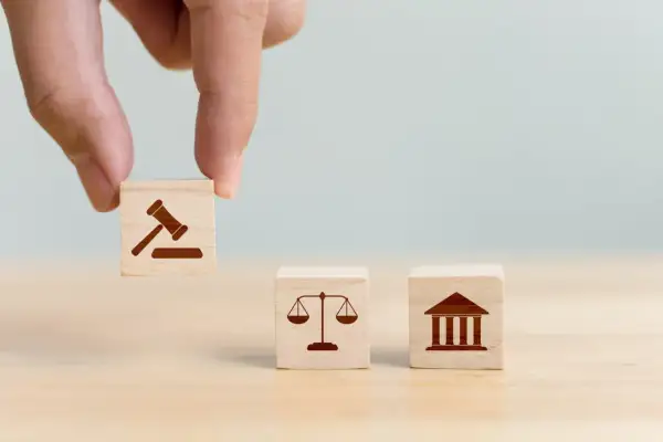 Dłoń układa kostki symbolizujące prawo, sprawiedliwość i sąd. Decyzja o jurysdykcji.